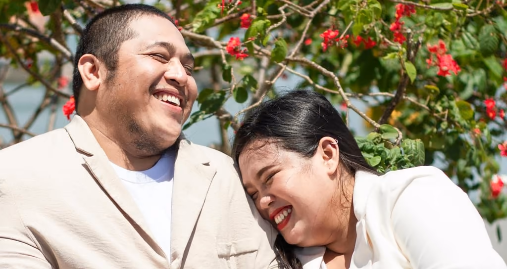 A couple in light-colored suits sitting outside and laughing together