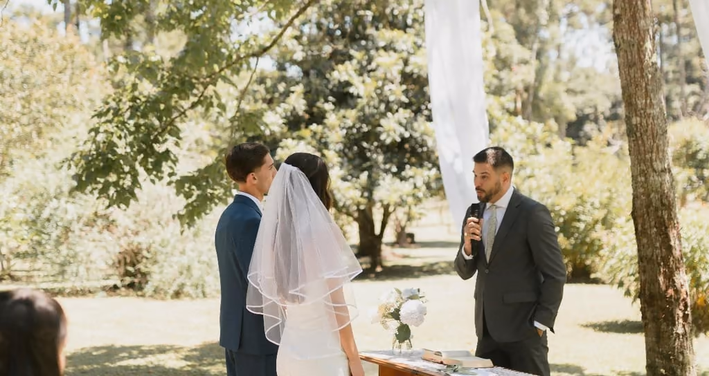 A bride and groom standing at an outdoor altar with an officiant under a large tree