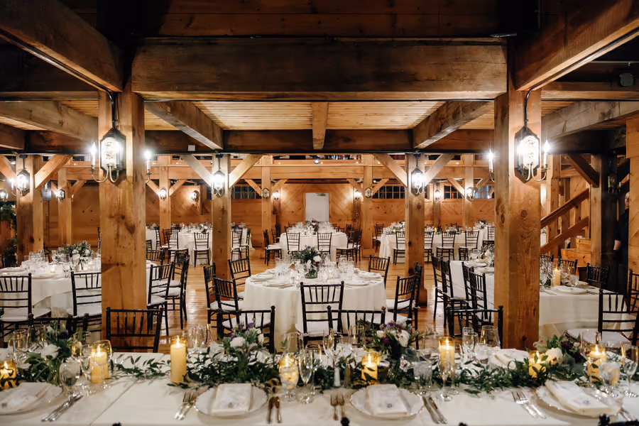 A barn reception hall set with round tables, candles, and hanging pendant lights