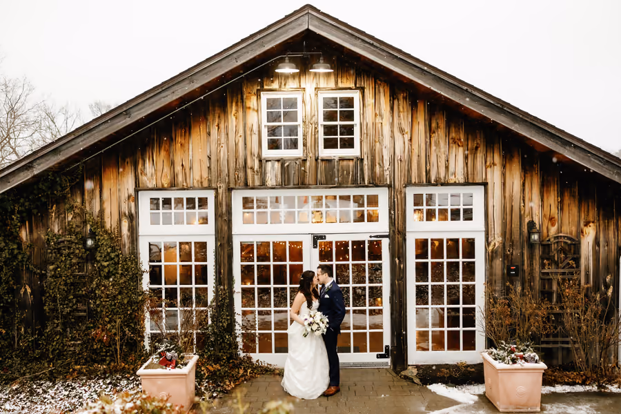 A couple embracing outside a rustic barn wedding venue with tall windows