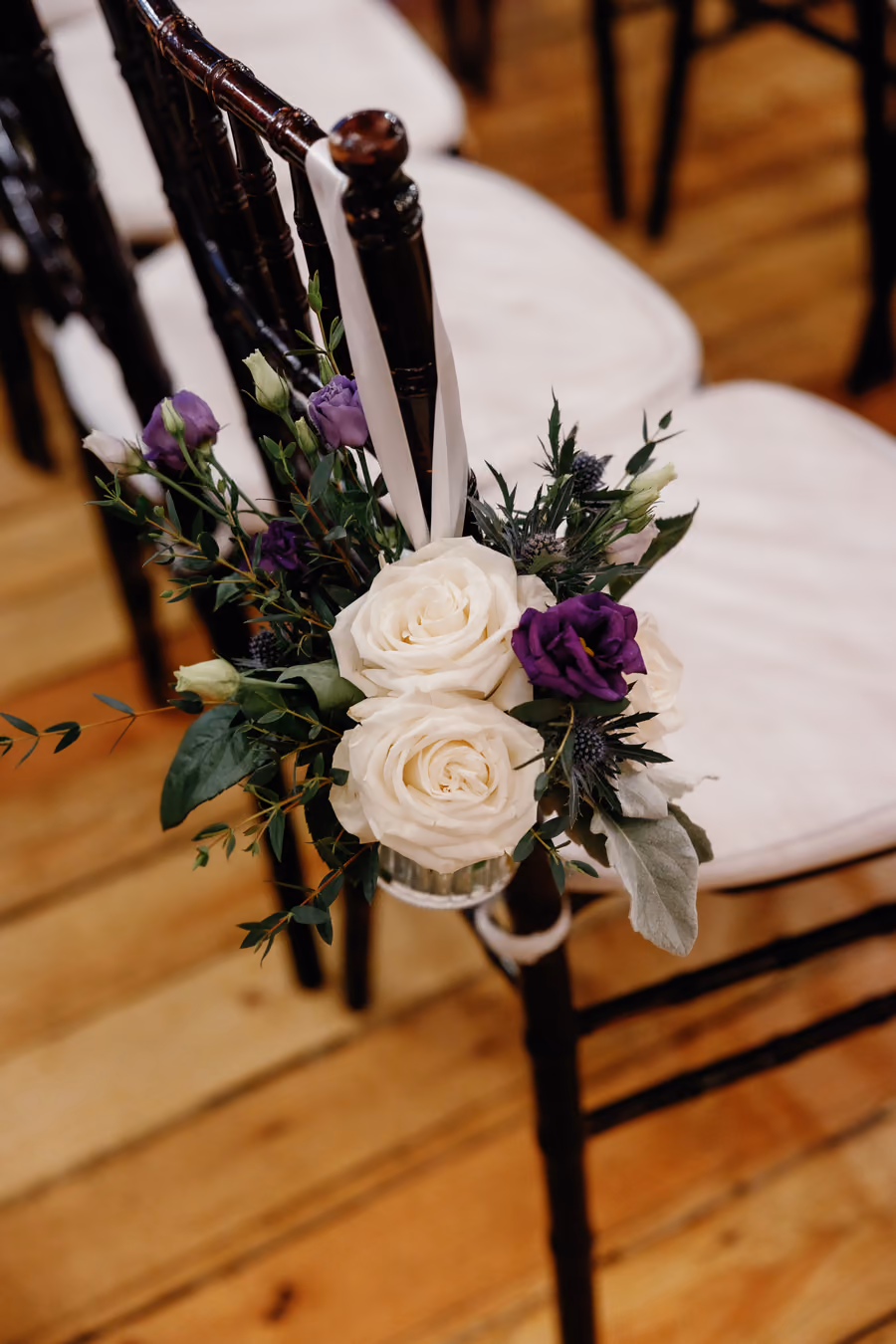 A bridal bouquet of white roses with deep purple accents resting on a chair