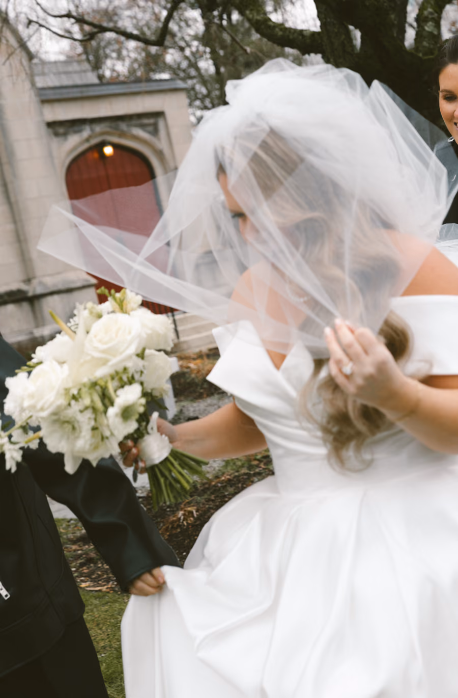 A bride in a long veil holding a white bouquet, photographed from behind