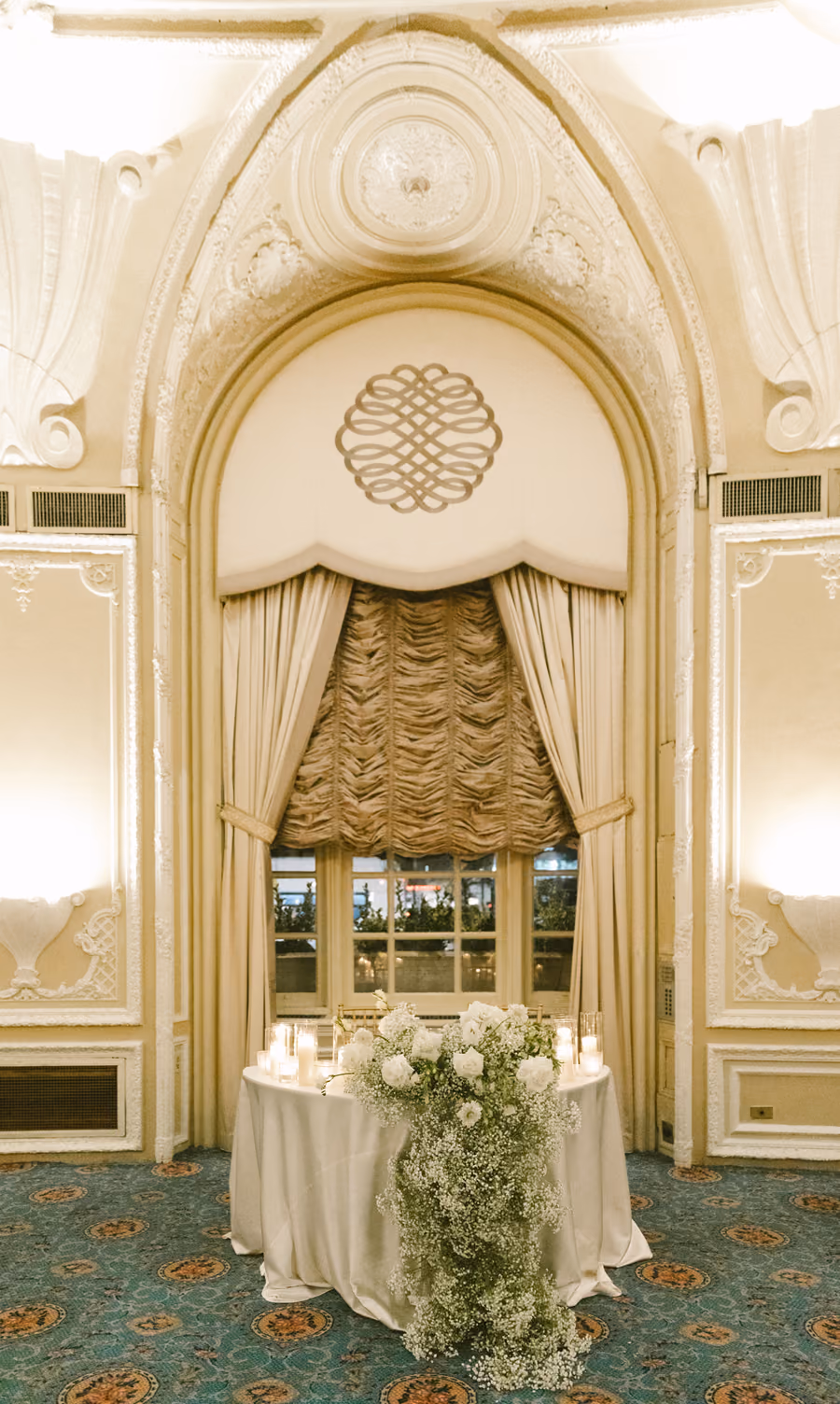 An ornate ballroom window framed by gathered drapery and gold detailing