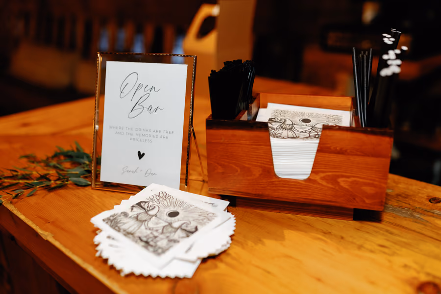 An open bar sign beside printed drink menus on a wooden bar