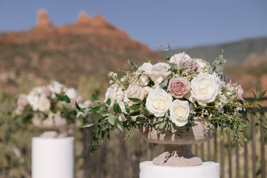 A wedding cake decorated with blush and white flowers against a red rock backdrop