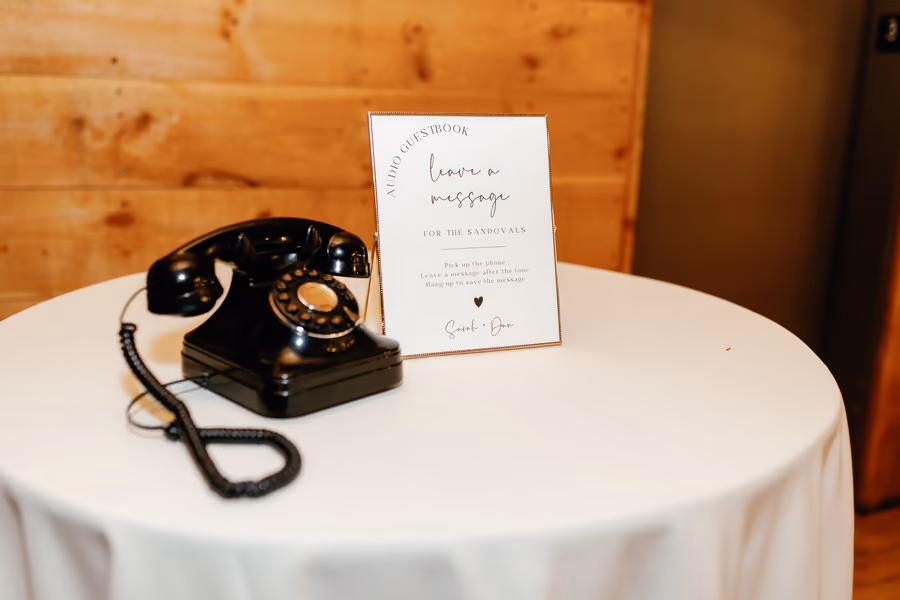 A vintage black rotary phone set up as an audio guestbook beside a printed sign