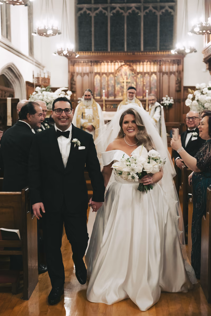 A smiling bride and groom walking down the aisle of a church after their wedding ceremony