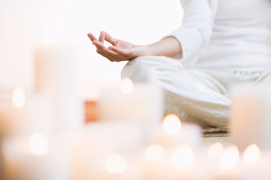 A person sitting cross-legged in a meditative pose surrounded by lit pillar candles