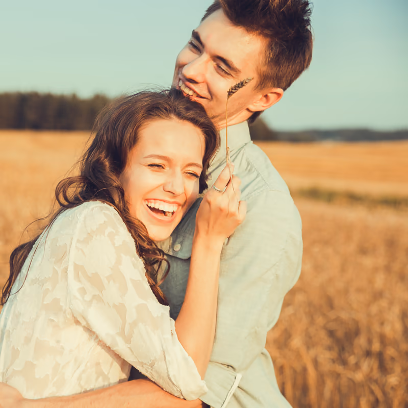 A couple hugging tightly and laughing in a sunlit field