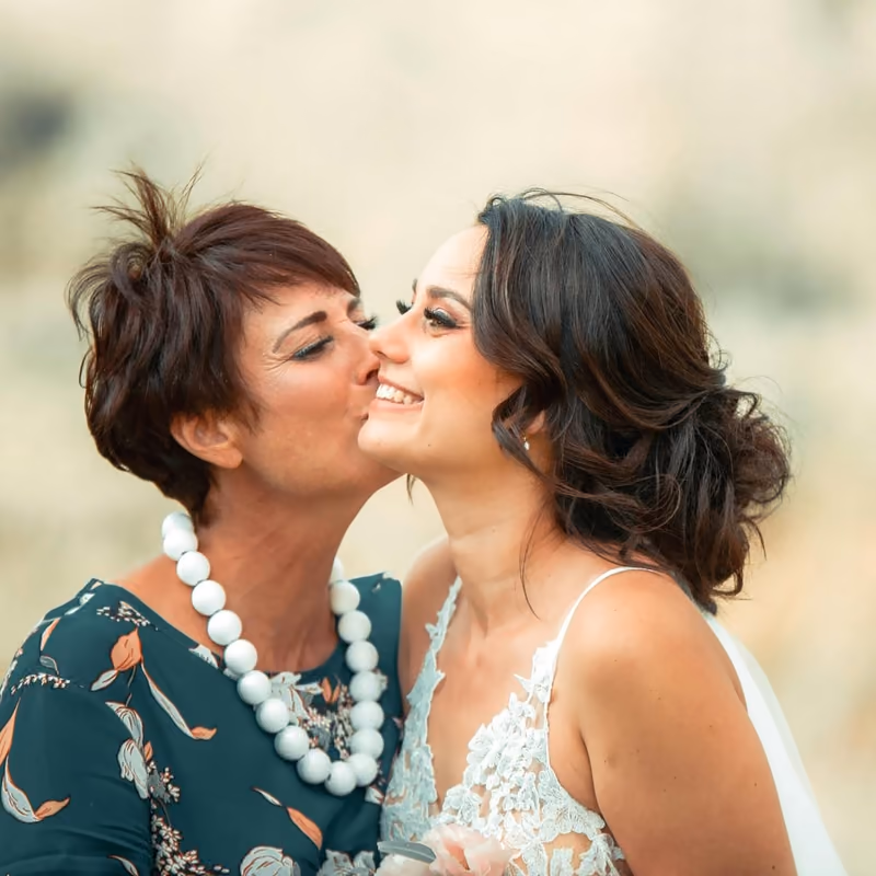 A mother kissing the smiling bride on the cheek while getting ready
