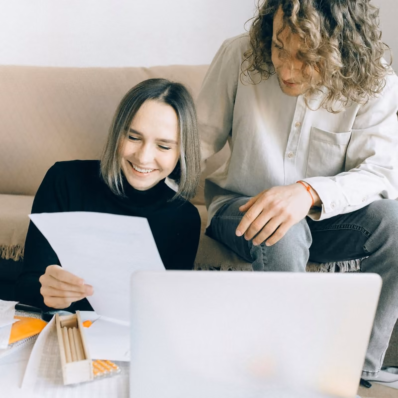 A couple smiling while looking at a laptop and paperwork together on the floor