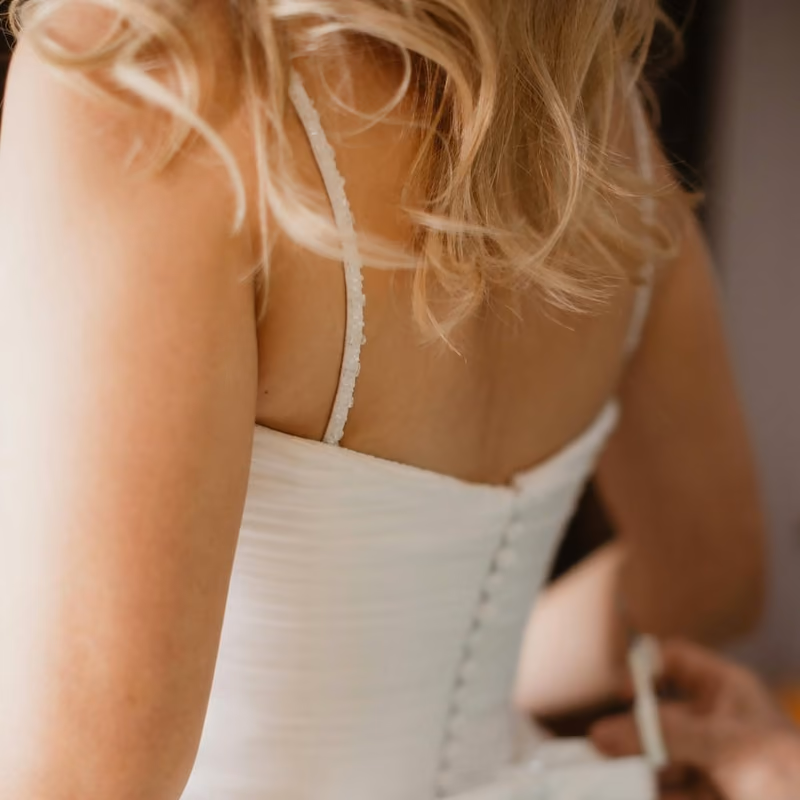 A close-up of a bride having the back of her white wedding dress tied