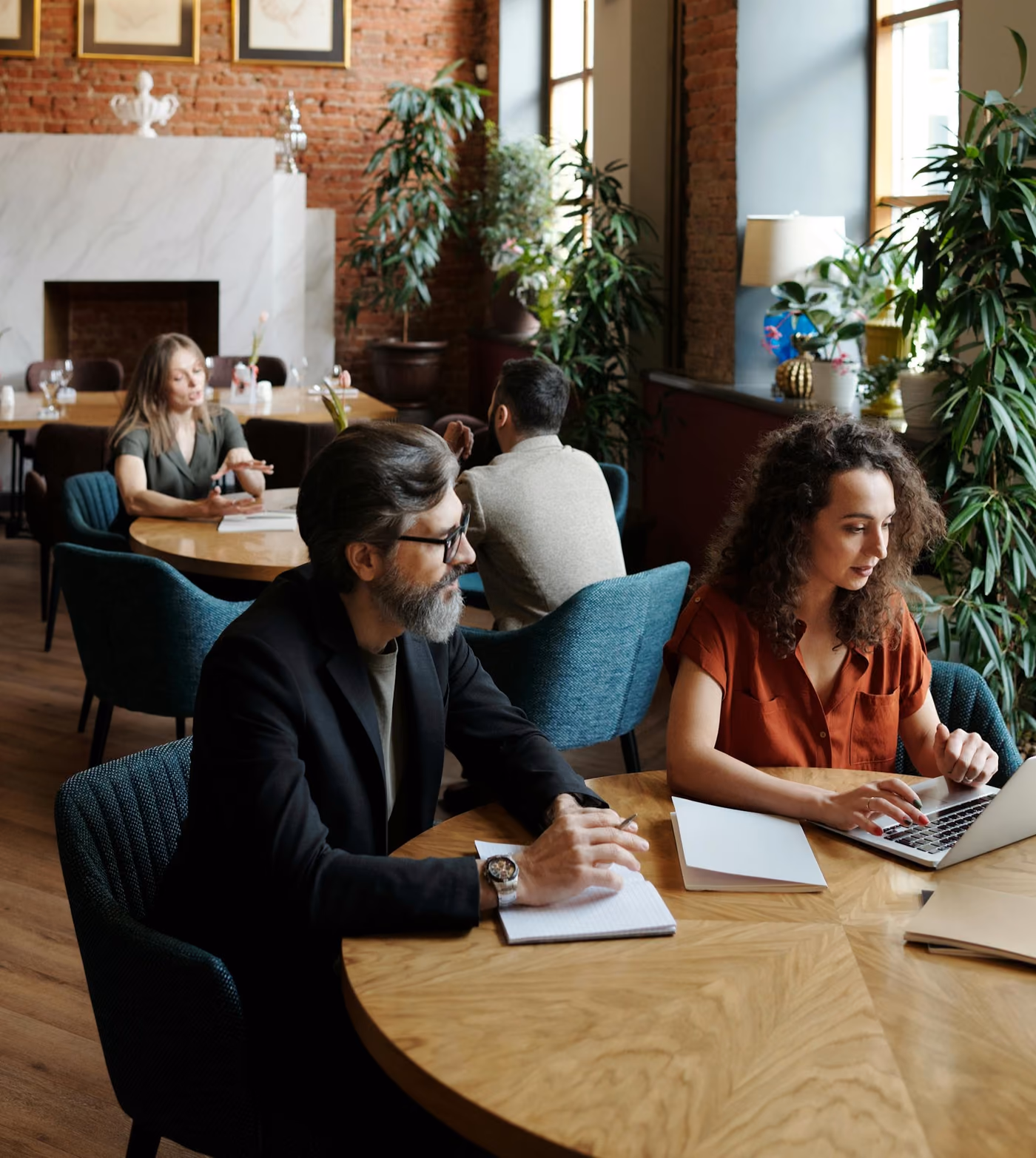 A group of people working on laptops and notebooks at a long wooden table in a well-lit space